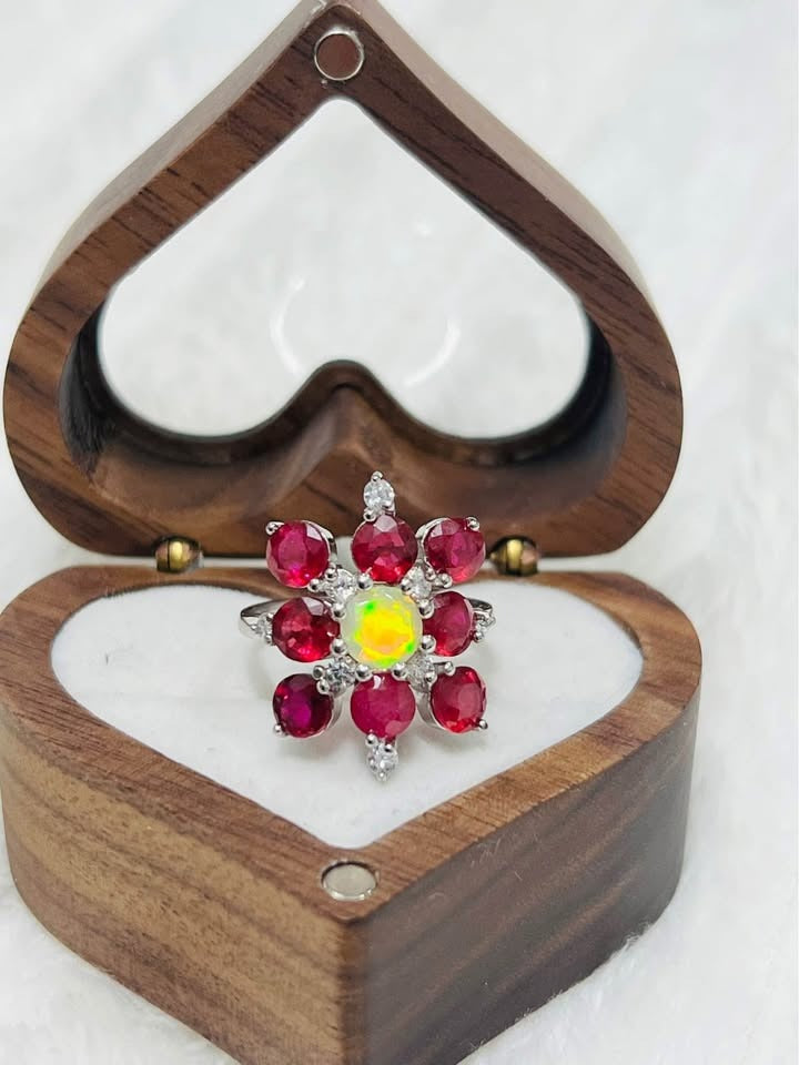 A sterling silver ring with a vibrant fire opal center and a halo of natural rubies, in a wooden heart-shaped box.