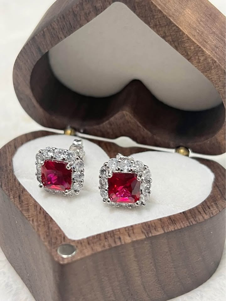Angled shot of brilliant sterling silver ruby stud earrings, framed by a heart-shaped wooden jewelry box.