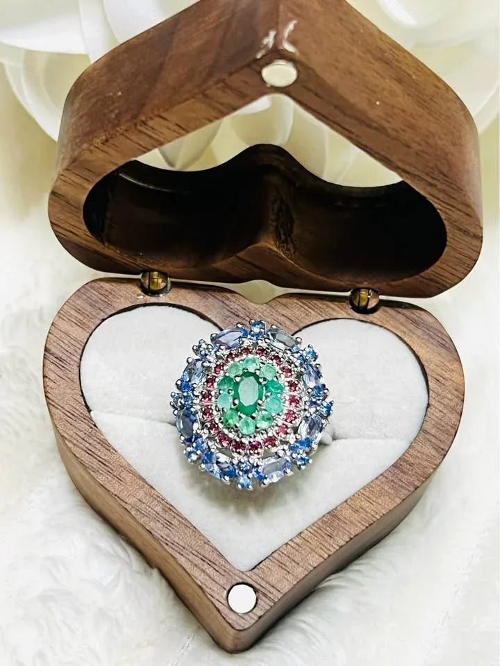 A stunning ring with emerald, rhodolite garnet, and tanzanite gemstones, showcased in a heart-shaped wooden box.