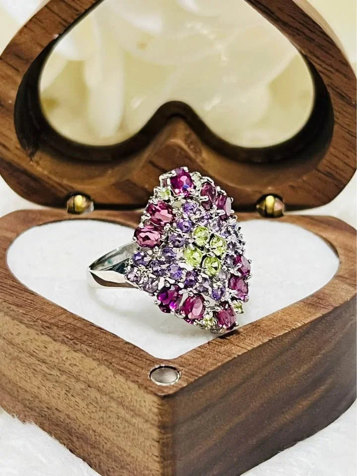 Side view of a stunning ring with rhodolite, amethyst, and peridot gems in a heart-shaped wooden box.