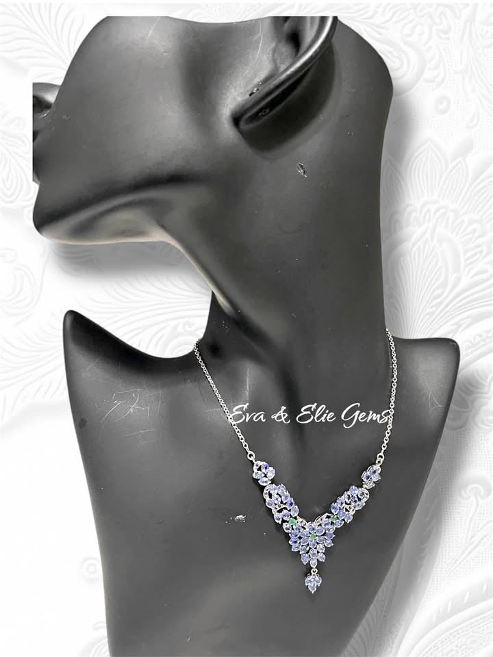 Side view of a silver necklace featuring a cluster of tanzanite and a touch of emerald. Shows the elegant drape and length.