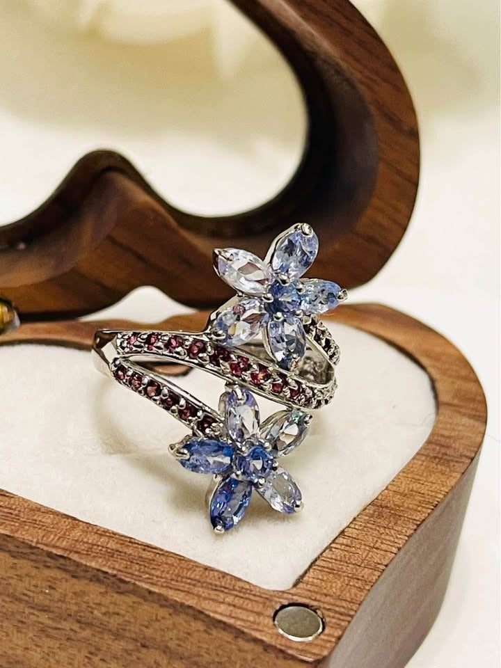 A 925 silver ring featuring two tanzanite flower clusters and a curved band of rhodolite gemstones.