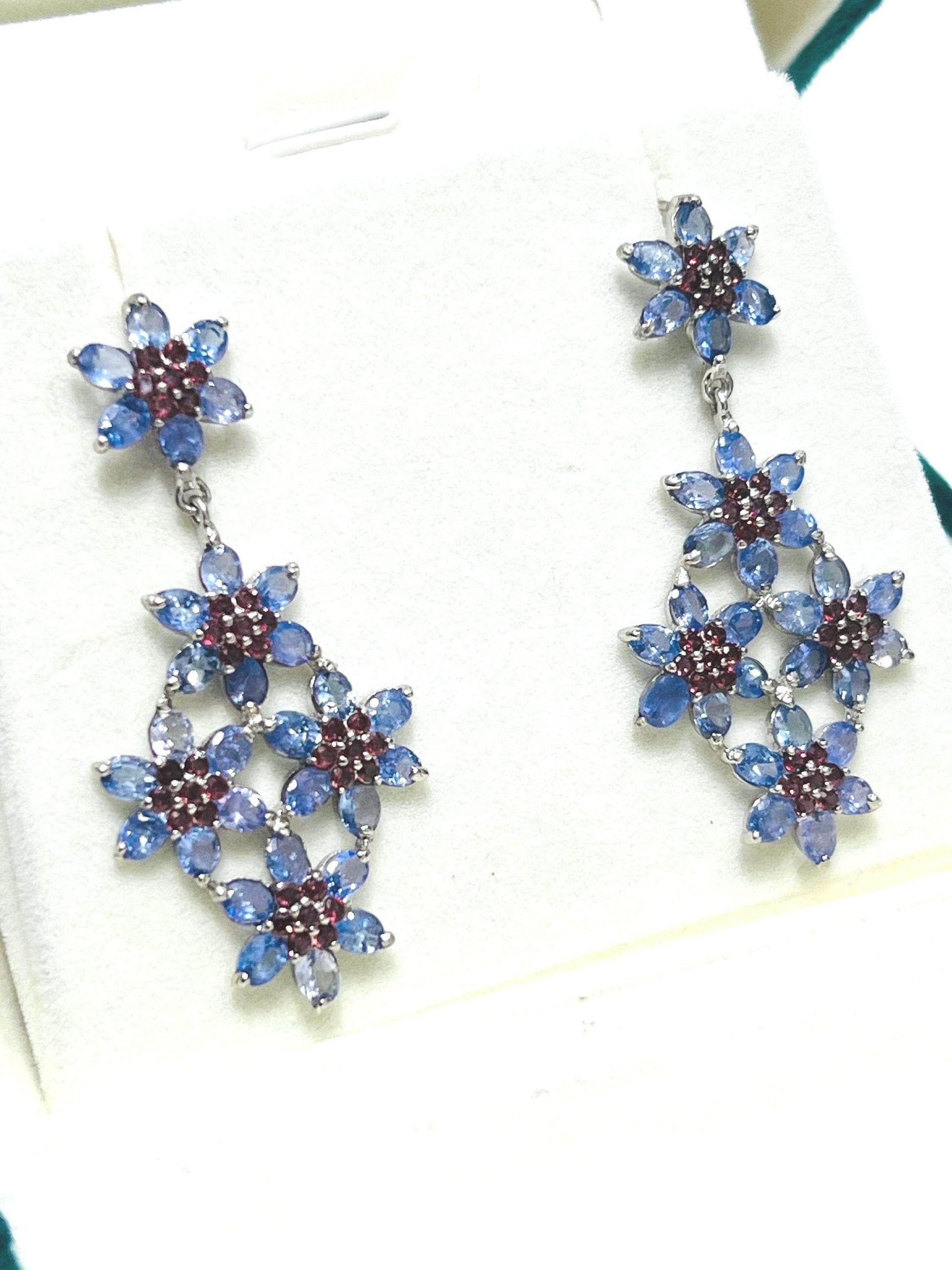 Detailed view of striking floral dangle earrings featuring clusters of tanzanite and garnet gemstones.