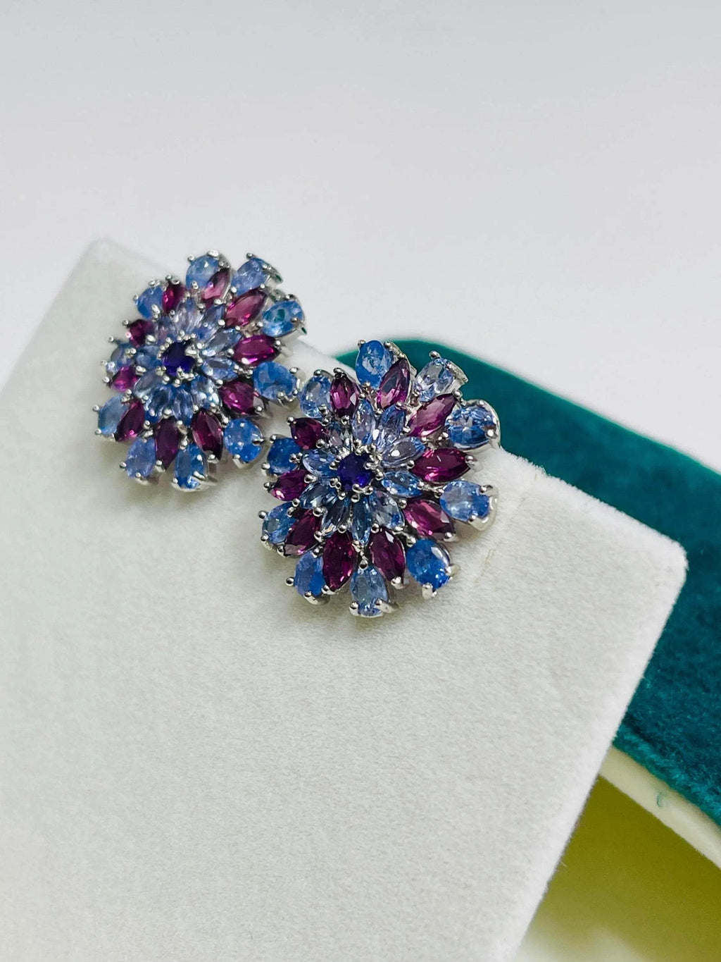 Angled view of sparkling tanzanite and rhodolite sunburst earrings, showcasing intricate design and rich colors.
