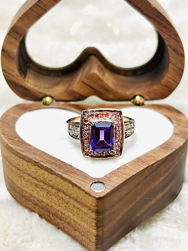  Close-up of a vibrant natural amethyst ring with a diamond halo and red accent gems.