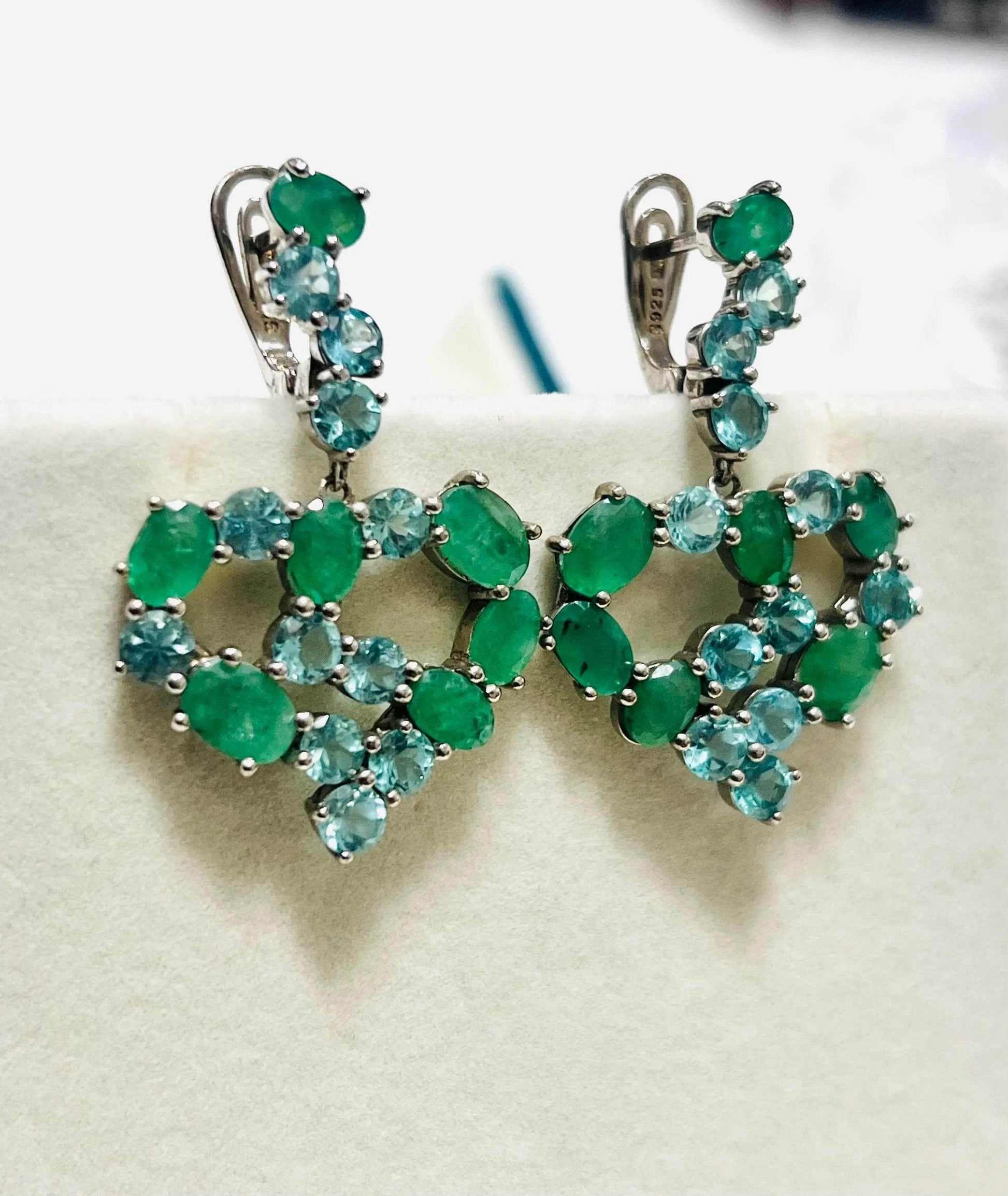 Pair of vintage-style heart-shaped dangle earrings with natural emeralds and blue apatite on display.