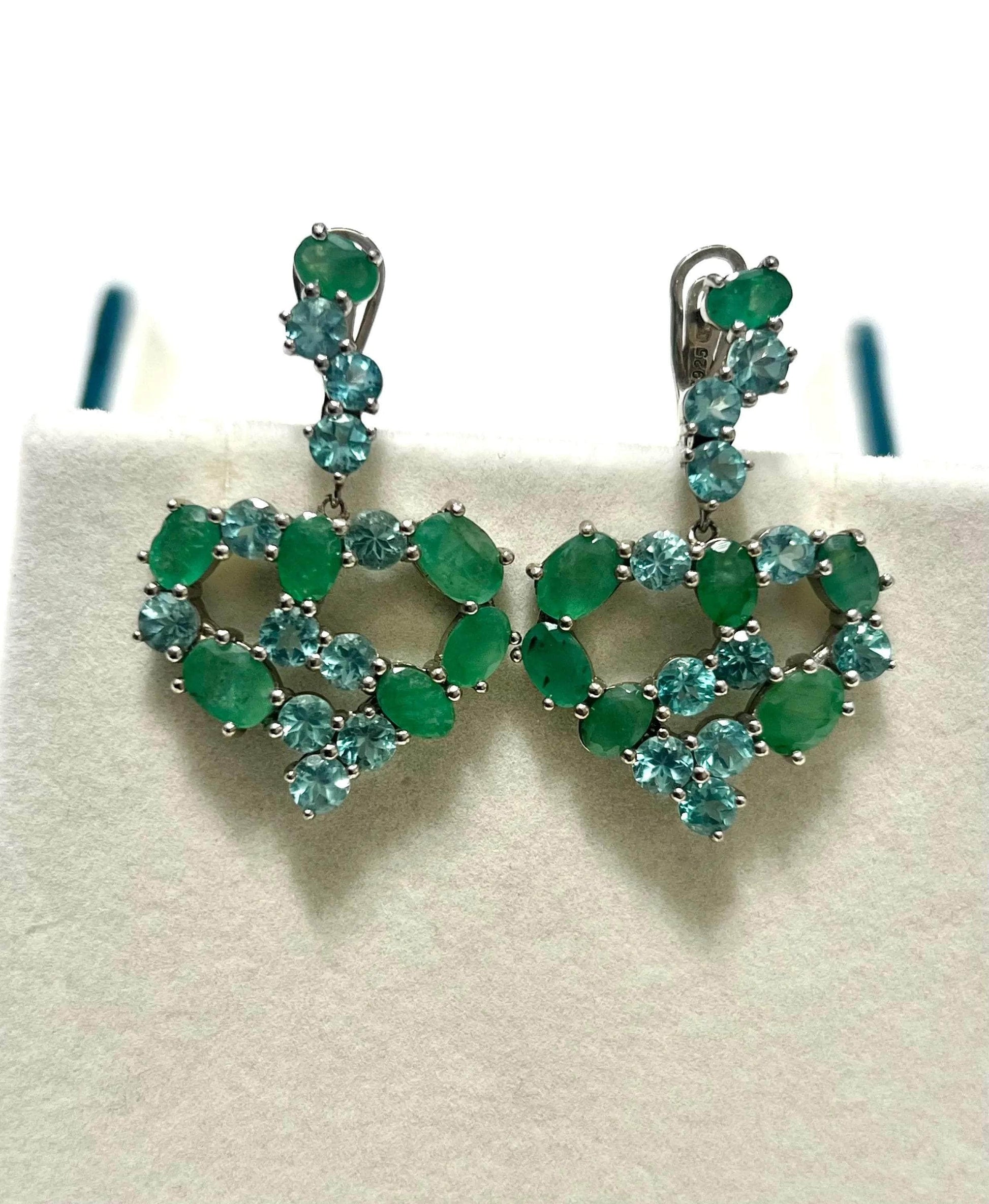 Full frontal view of beautiful vintage emerald and apatite heart-shaped earrings on a white jewelry stand.
