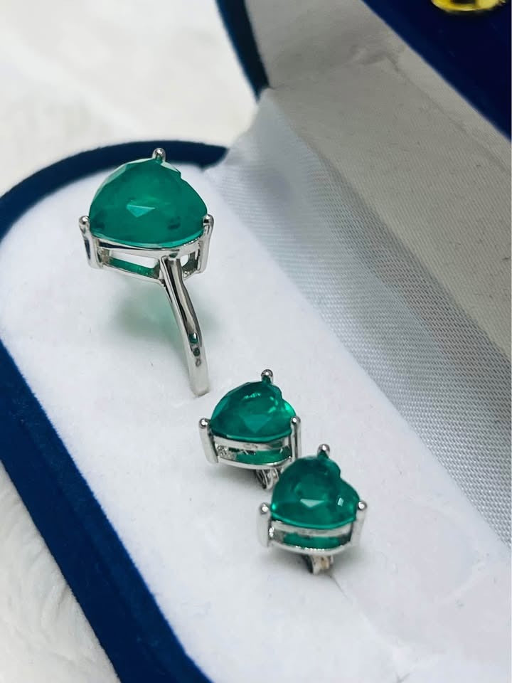 Angled view of dainty Zambian emerald heart ring and earrings in sterling silver setting.